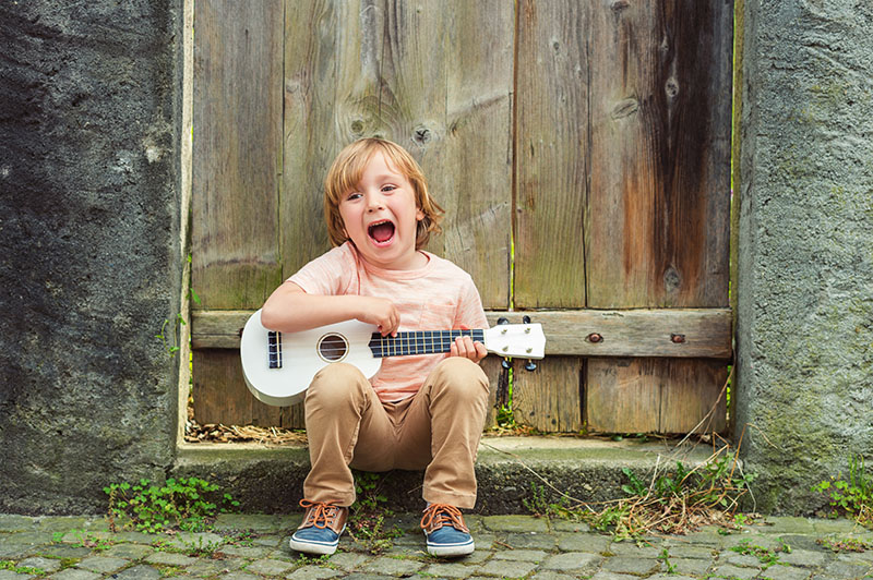 Young boy singing and playing guitar, sitting on a door stoop.